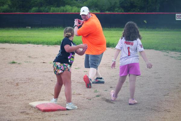 Monitor Photo/ Russell Slaton  Kemp High School head softball coach Kristopher Hutchins gives Kemp ISD students Lacie Olivarez (foreground, from left) and Emilynn Morris some wise words of advice: step into the swing. This night’s event (July 16) was the closing chapter of the June 8-July 16 Kemp summer athletic clinics.