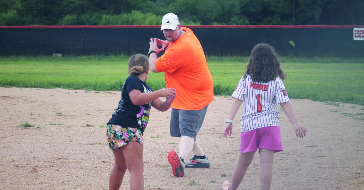 Monitor Photo/ Russell Slaton  Kemp High School head softball coach Kristopher Hutchins gives Kemp ISD students Lacie Olivarez (foreground, from left) and Emilynn Morris some wise words of advice: step into the swing. This night’s event (July 16) was the closing chapter of the June 8-July 16 Kemp summer athletic clinics.
